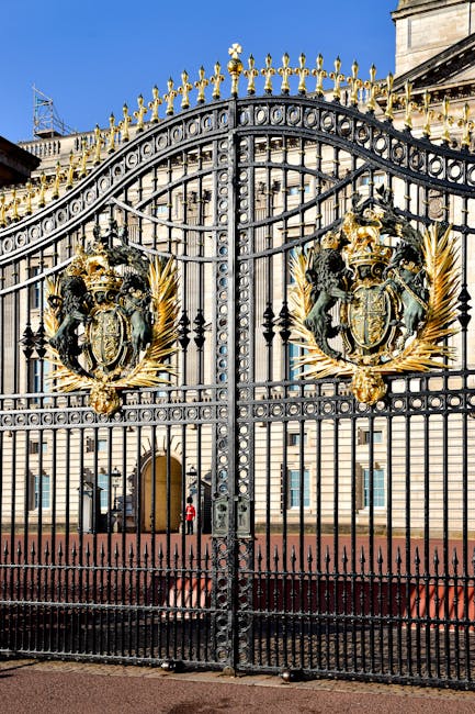 A large, ornate wrought iron gate featuring intricate design elements and decorative gold accents, including heraldic shields and gilded leaf motifs. The gate is painted black with a weathered texture