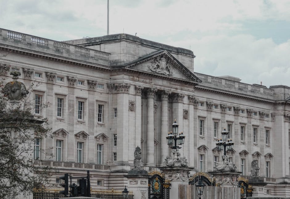 A large, ornate wrought iron gate featuring intricate design elements and decorative gold accents, including heraldic shields and gilded leaf motifs. The gate is painted black with a weathered texture
